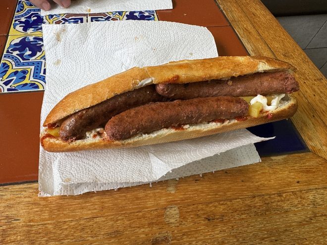 A grilled sausage baguette on a tiled table.