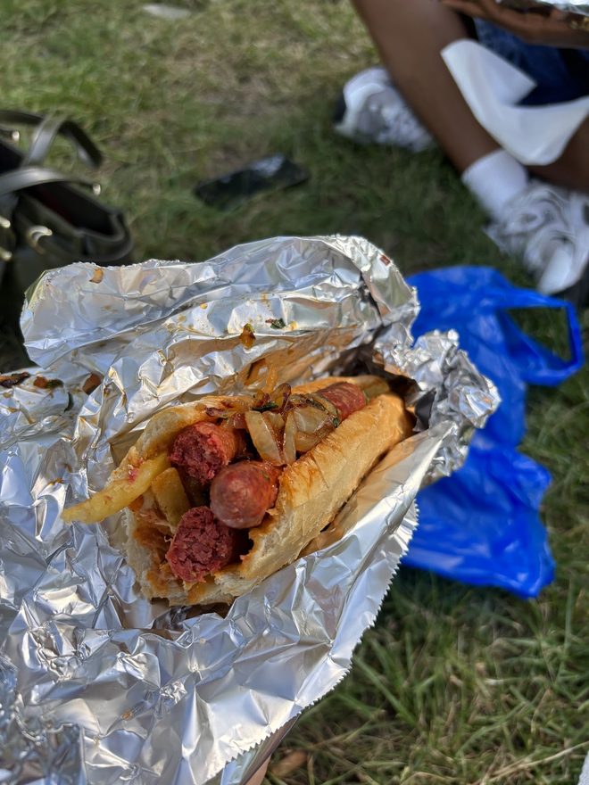 A sausage and potato sandwich held over the grass.