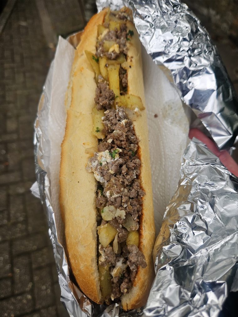 Overhead view of an open baguette packed with minced meat and potato in foil.
