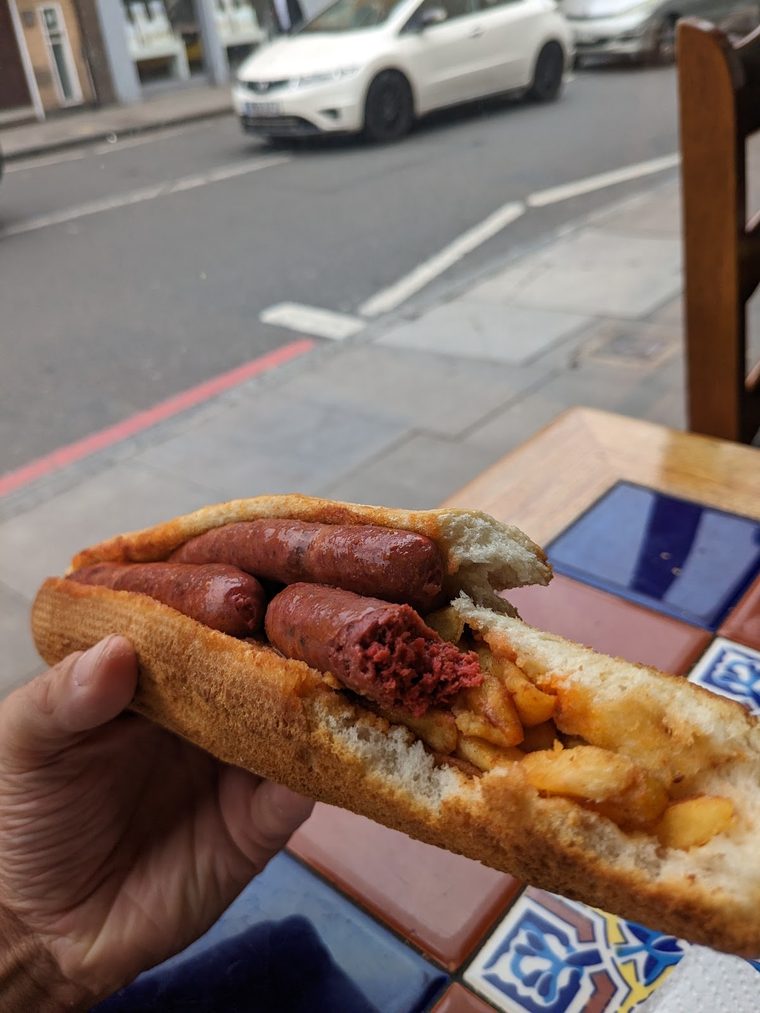 A sausage-and-chips baguette held on the street outside.